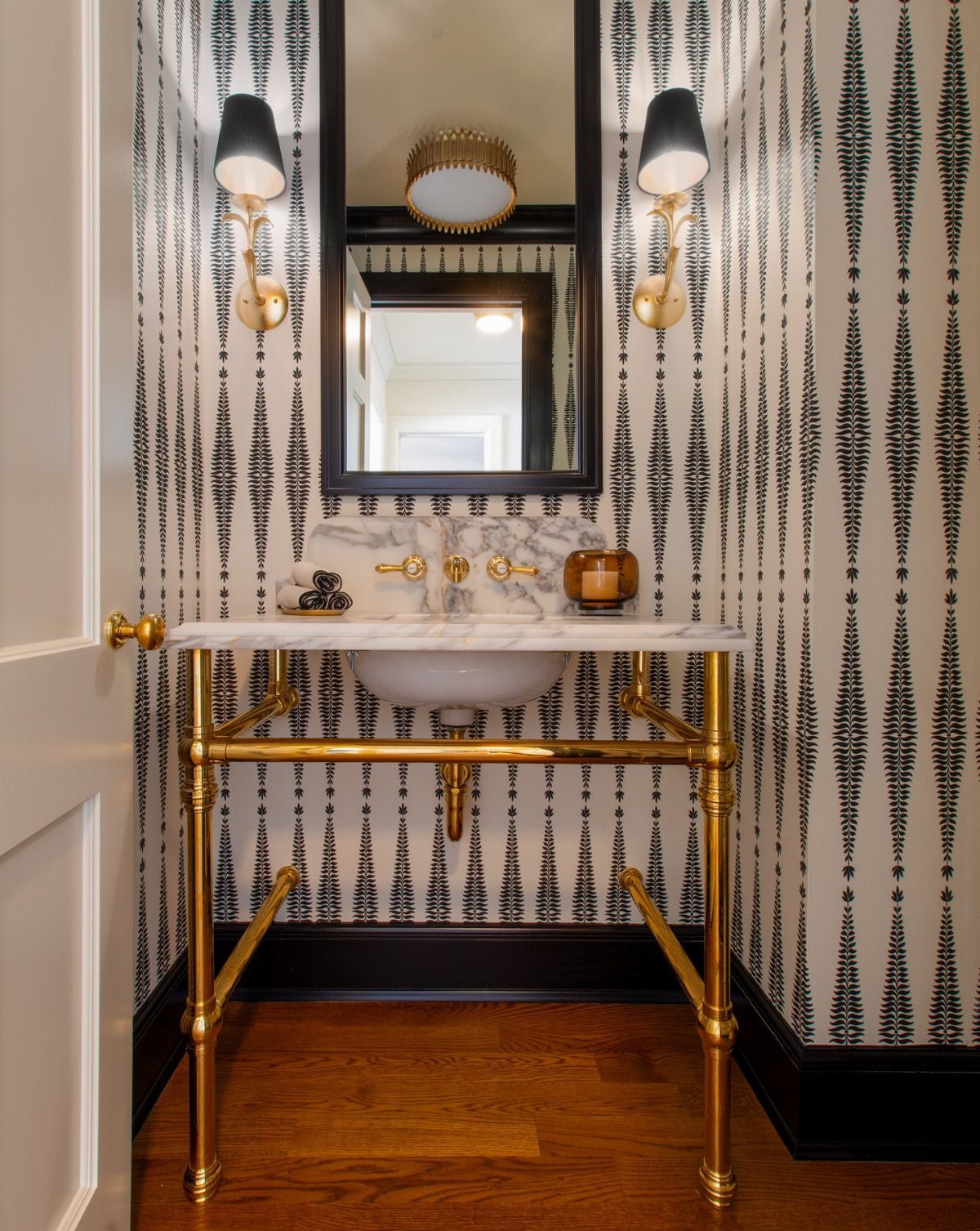 Gold wall sconces with black shades flanking a mirror in a patterned bathroom.