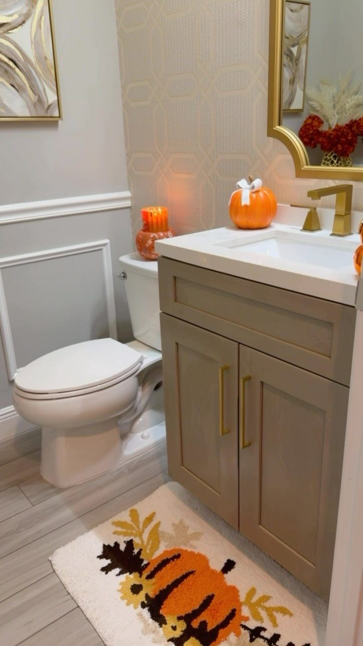 Small powder room with autumn decorations including a pumpkin and pumpkin-patterned rug.