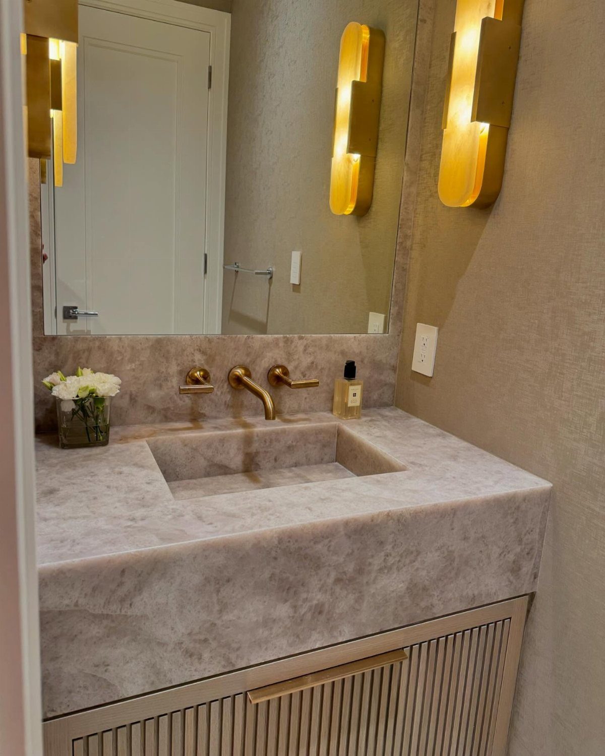 Integrated marble sink in a powder room with gold fixtures and warm lighting.