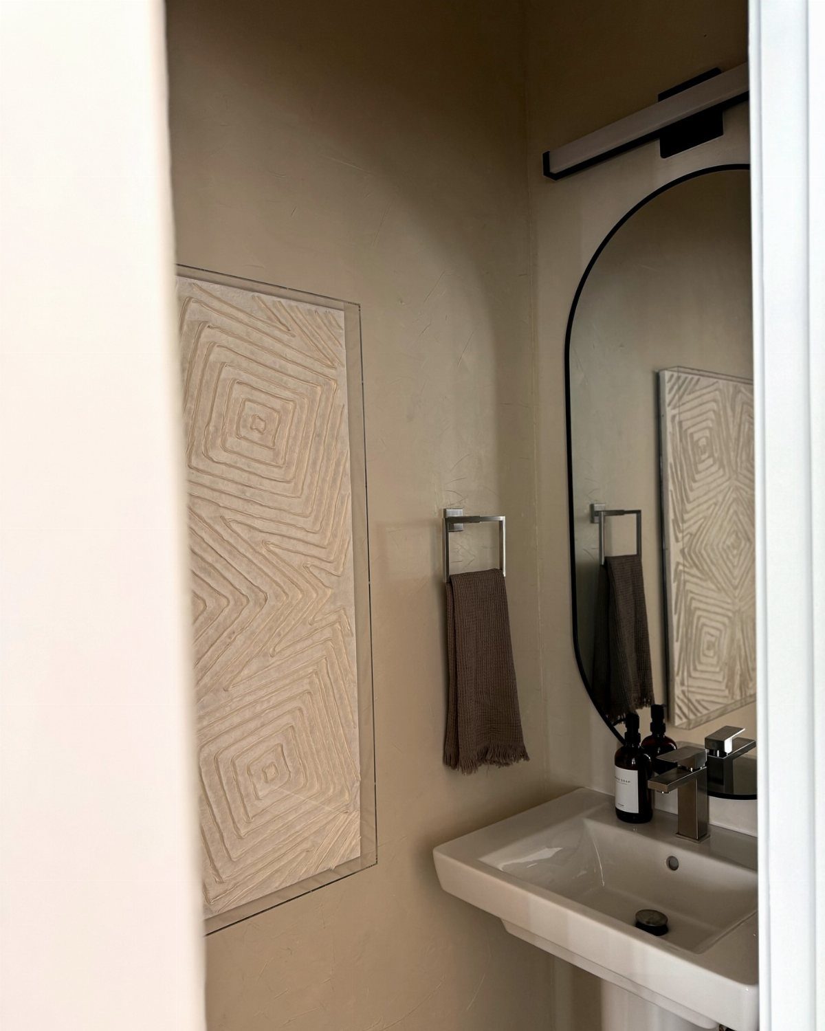 Small powder room with beige walls, white pedestal sink, and oval mirror.