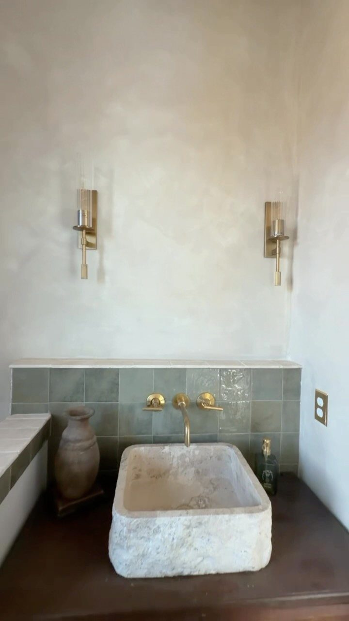 Stone vessel sink with gold fixtures in a small, modern powder room