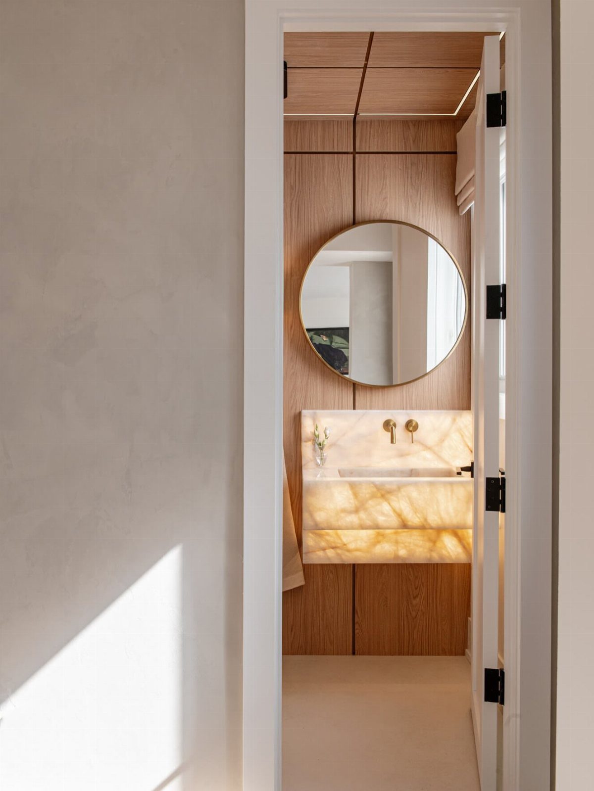 Small powder room with wood paneling, round mirror, and backlit onyx vanity.