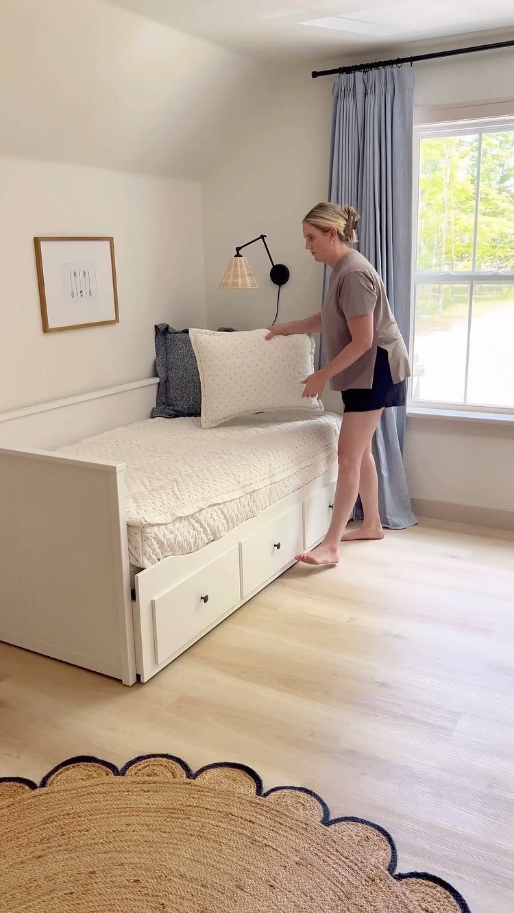 Woman arranging pillows on a white daybed with built-in storage drawers underneath.