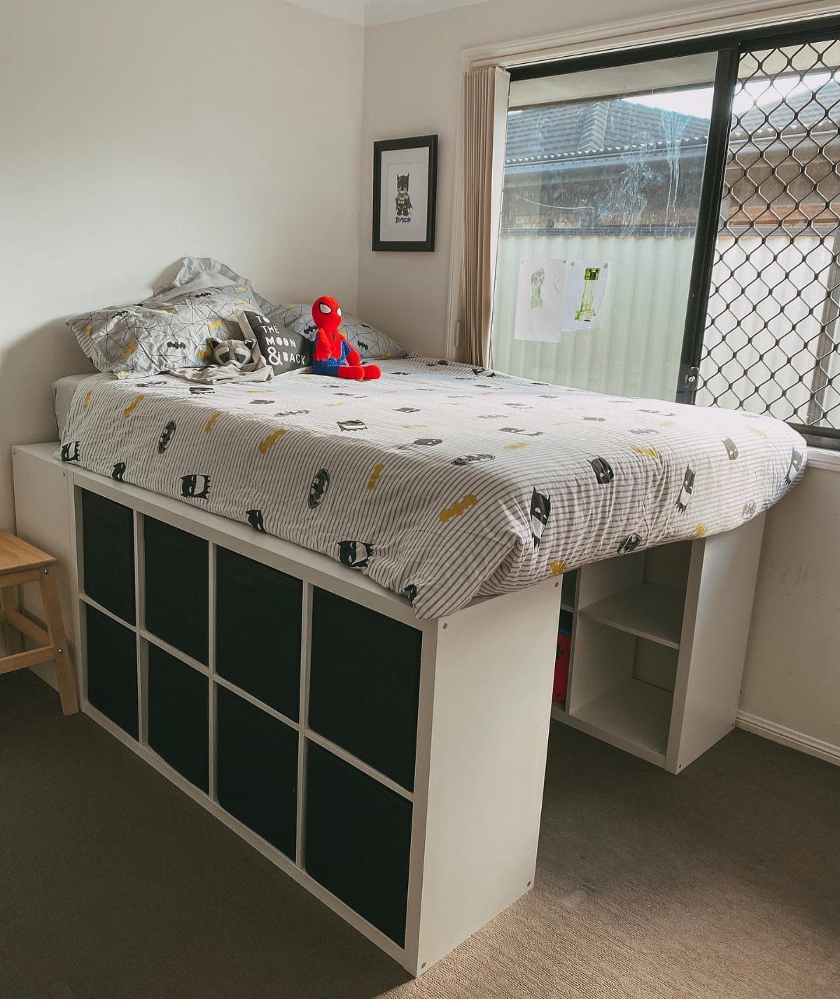Bed supported by a white shelving unit with black fabric storage bins underneath.