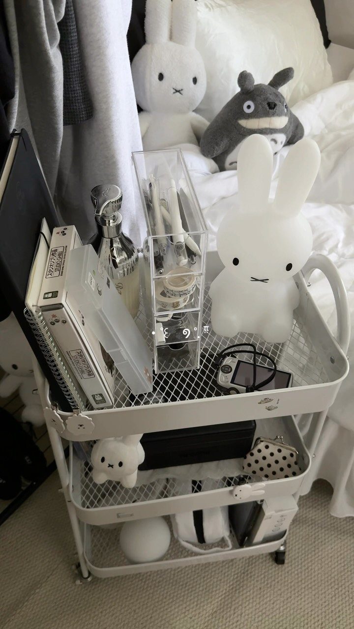 White three-tier rolling cart holding a bunny lamp and organizers in a bedroom.