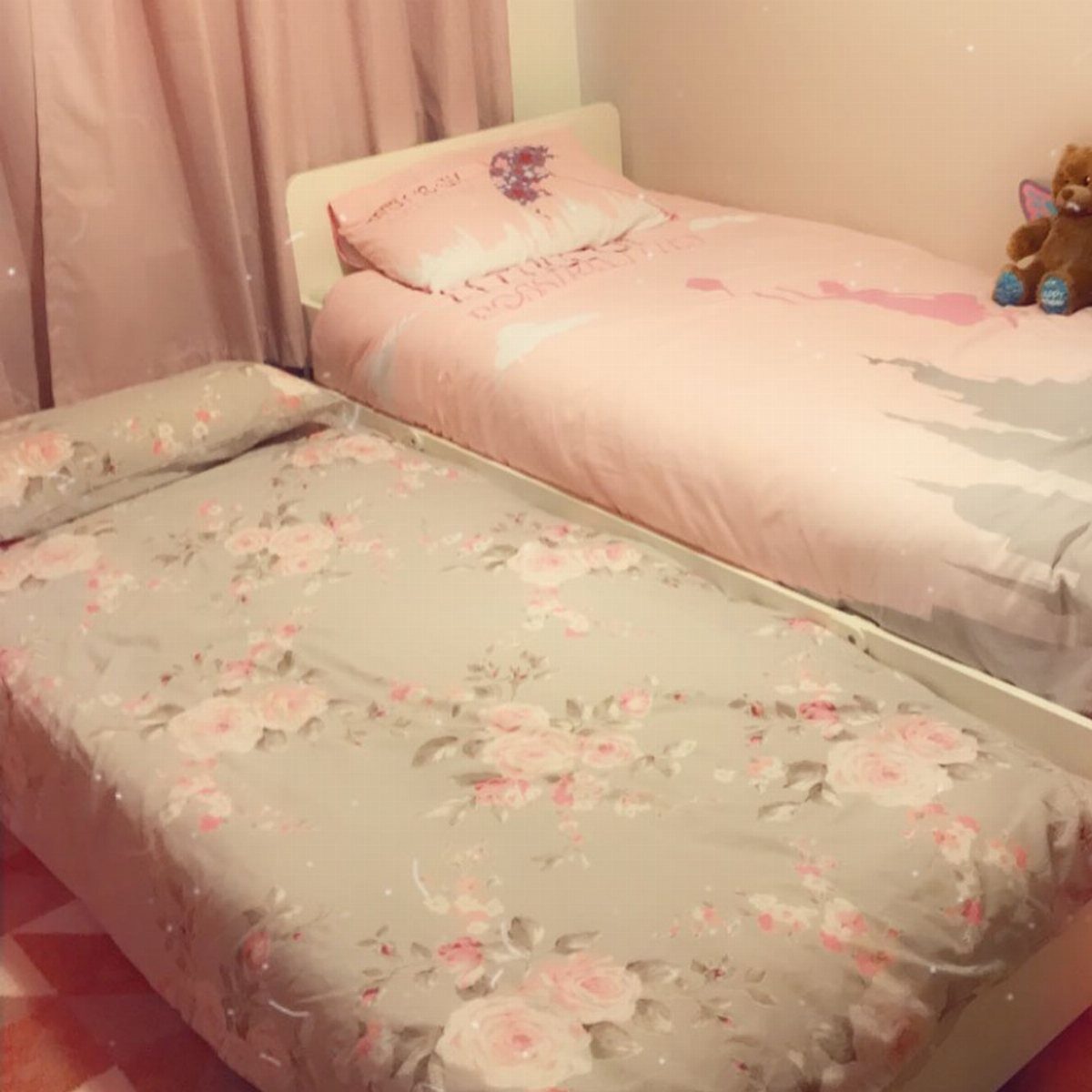 White trundle bed with pink and floral bedding in a small bedroom