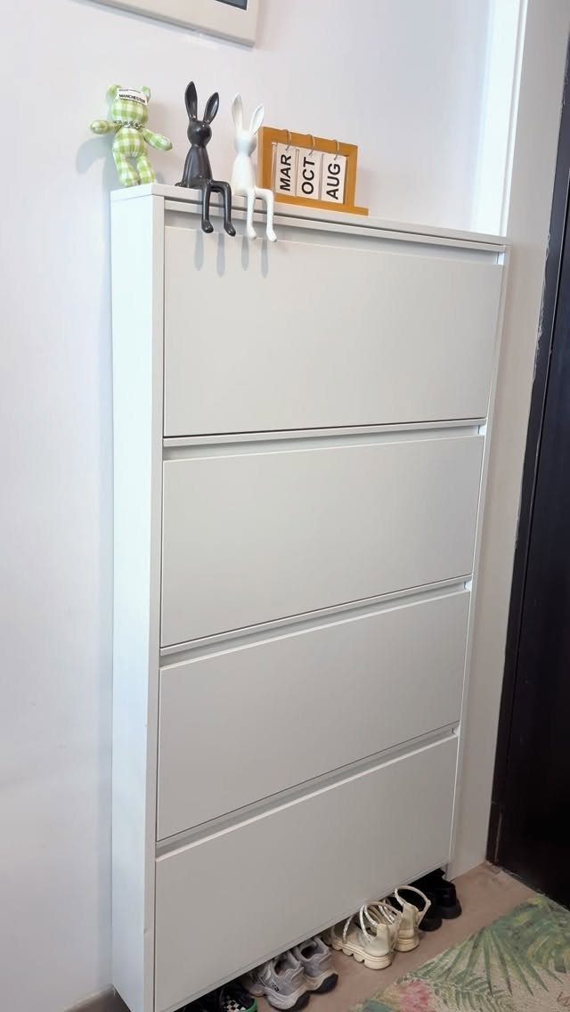 White slim shoe cabinet with decorative figurines and shoes on the floor.