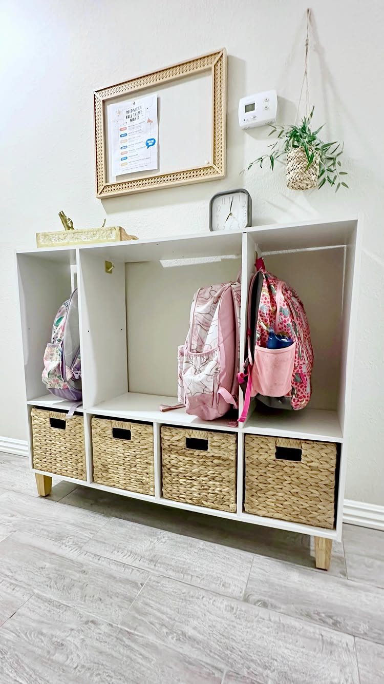 White cubby storage unit with woven baskets and backpacks in a small entryway.