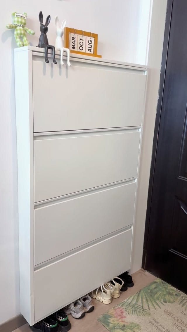White slim shoe cabinet with tilting drawers and shoes stored underneath by a door.