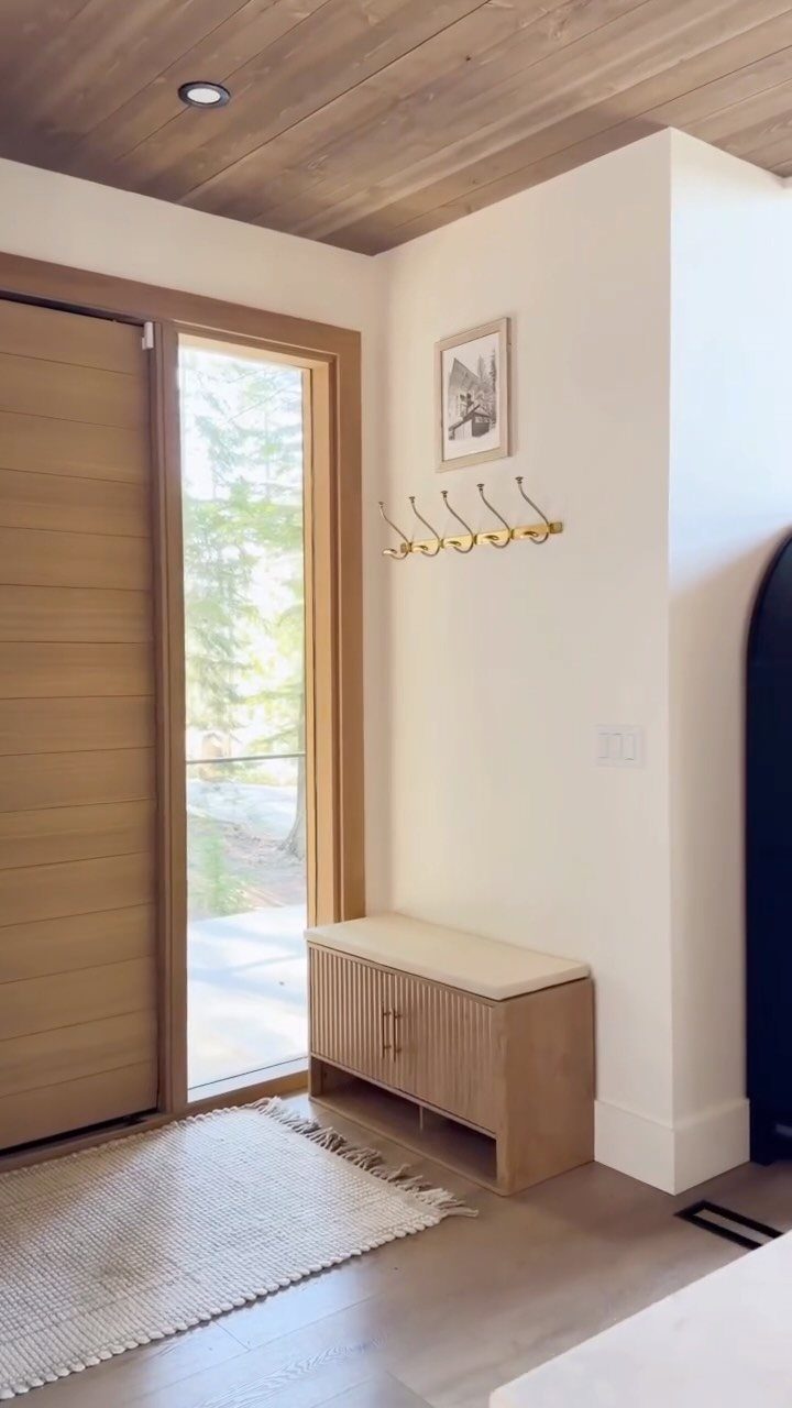 Light wood storage bench with cream cushion in a bright entryway with hooks.