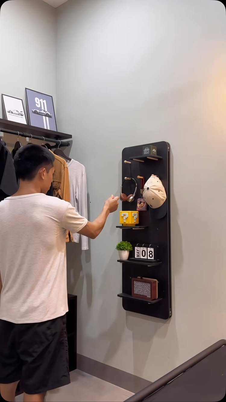 Man interacting with a black vertical wall organizer with shelves and hooks.
