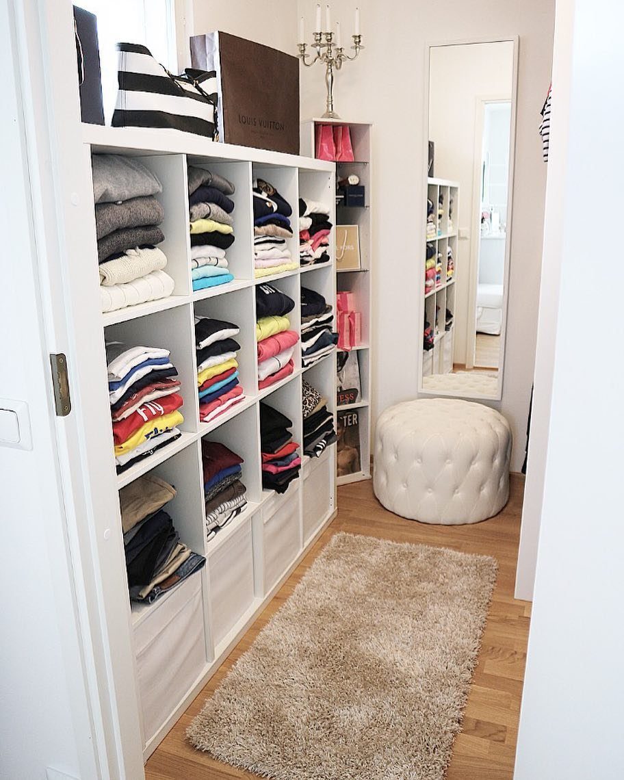 White open shelving unit with folded clothes, a mirror, and a beige rug.