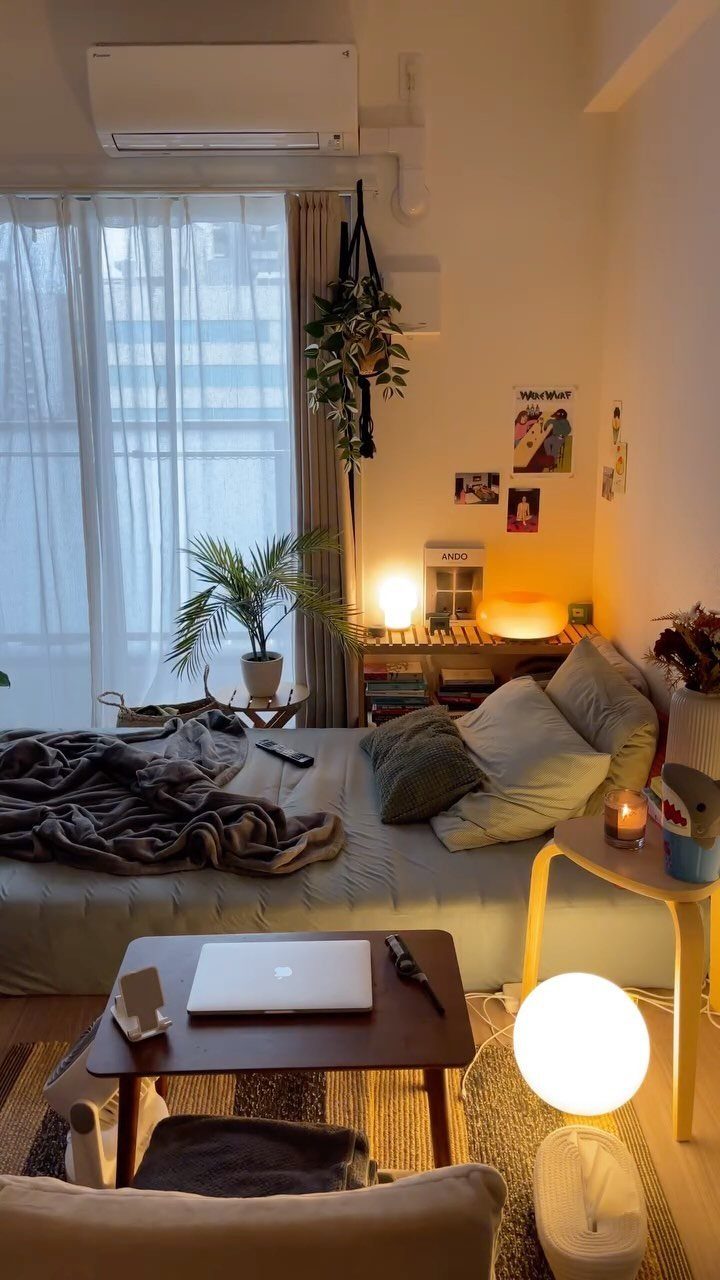 Small studio apartment with white walls, light curtains, and warm ambient lighting.