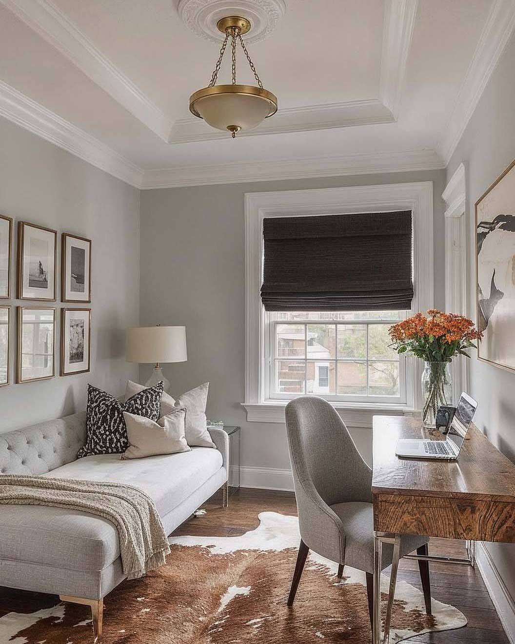 Tufted grey daybed and wooden desk in a small, light grey studio apartment.
