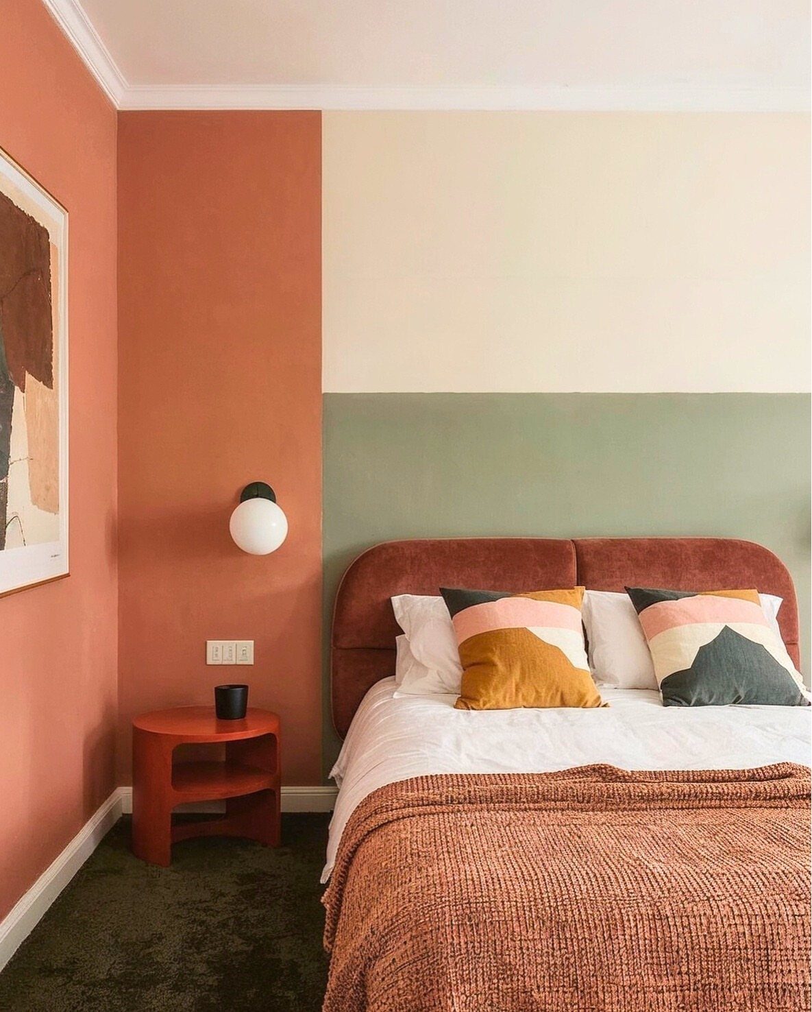 Bed with terracotta headboard, patterned pillows, and textured throw against color-blocked walls.