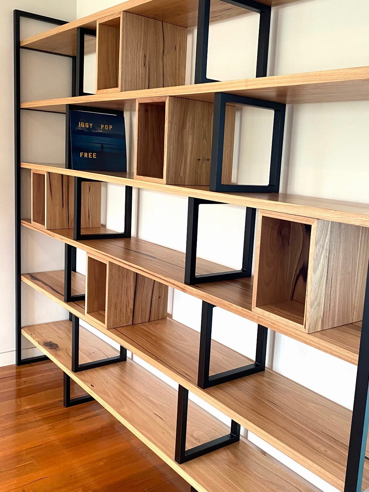 Tall modern shelving unit with light wood shelves and black metal frames.