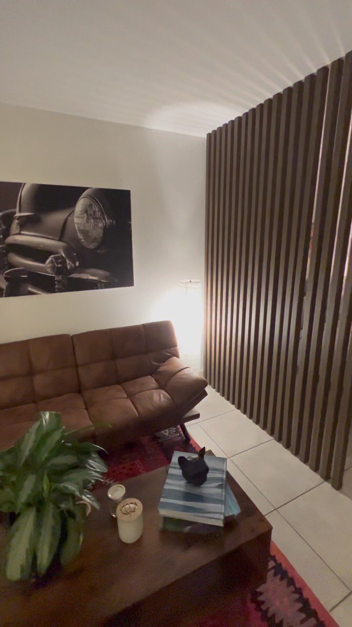 Wooden slat partition wall dividing a living room with a brown leather sofa.