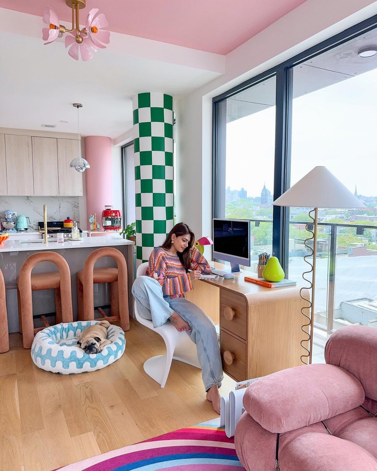 Bright studio apartment featuring a pink ceiling, checkered pillar, and colorful modern furniture.