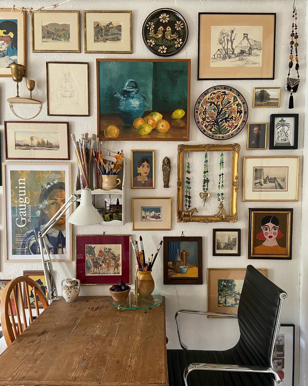 Gallery wall with various framed artworks and plates above a wooden desk