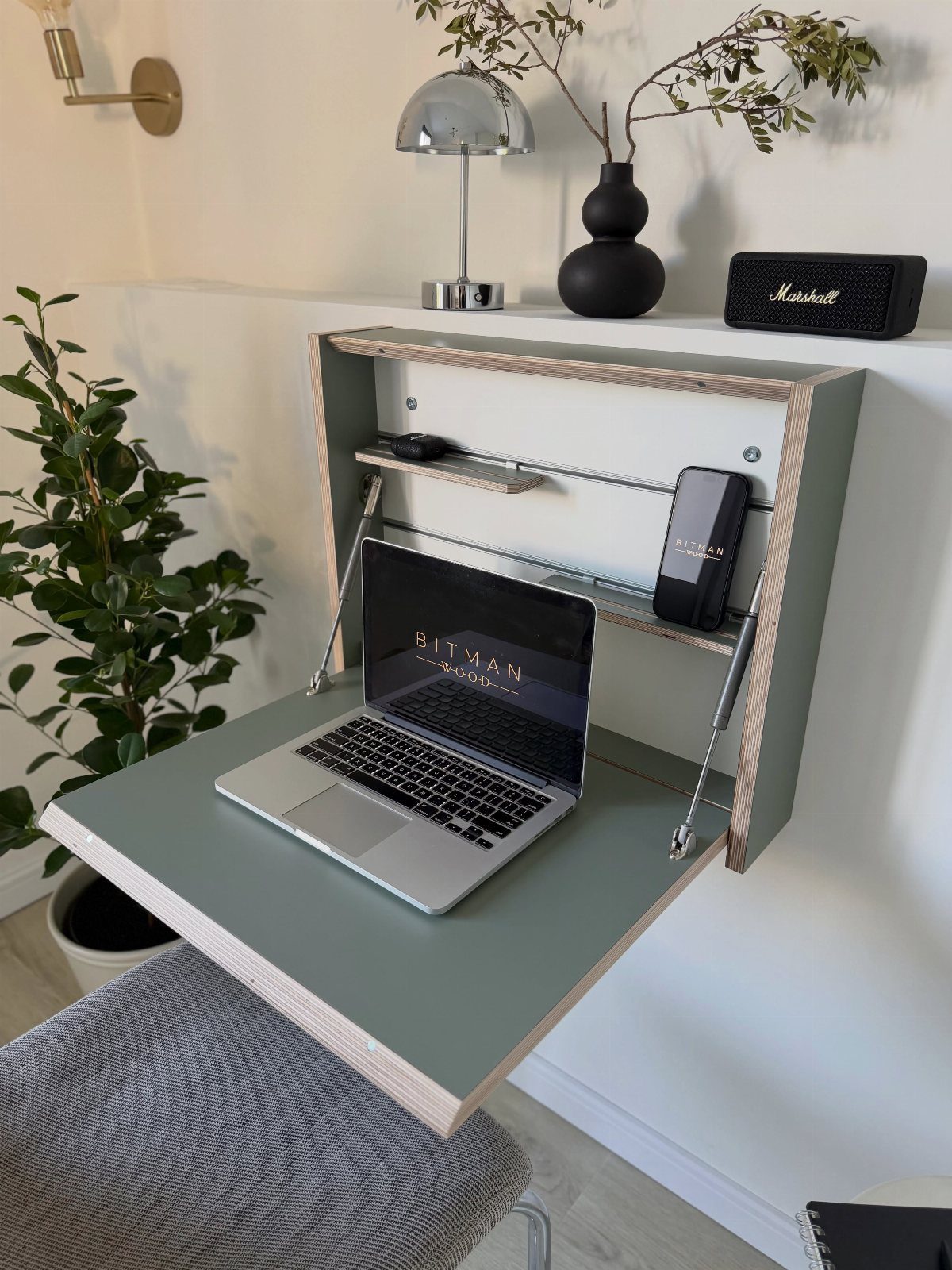 Wall-mounted folding desk with a laptop, small shelf, and minimalist decor accessories.