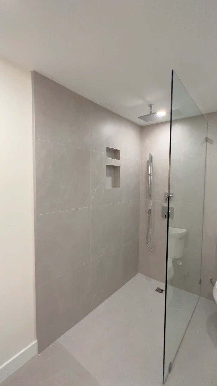 Curbless walk-in shower with grey tiles, glass partition, and a rain showerhead.
