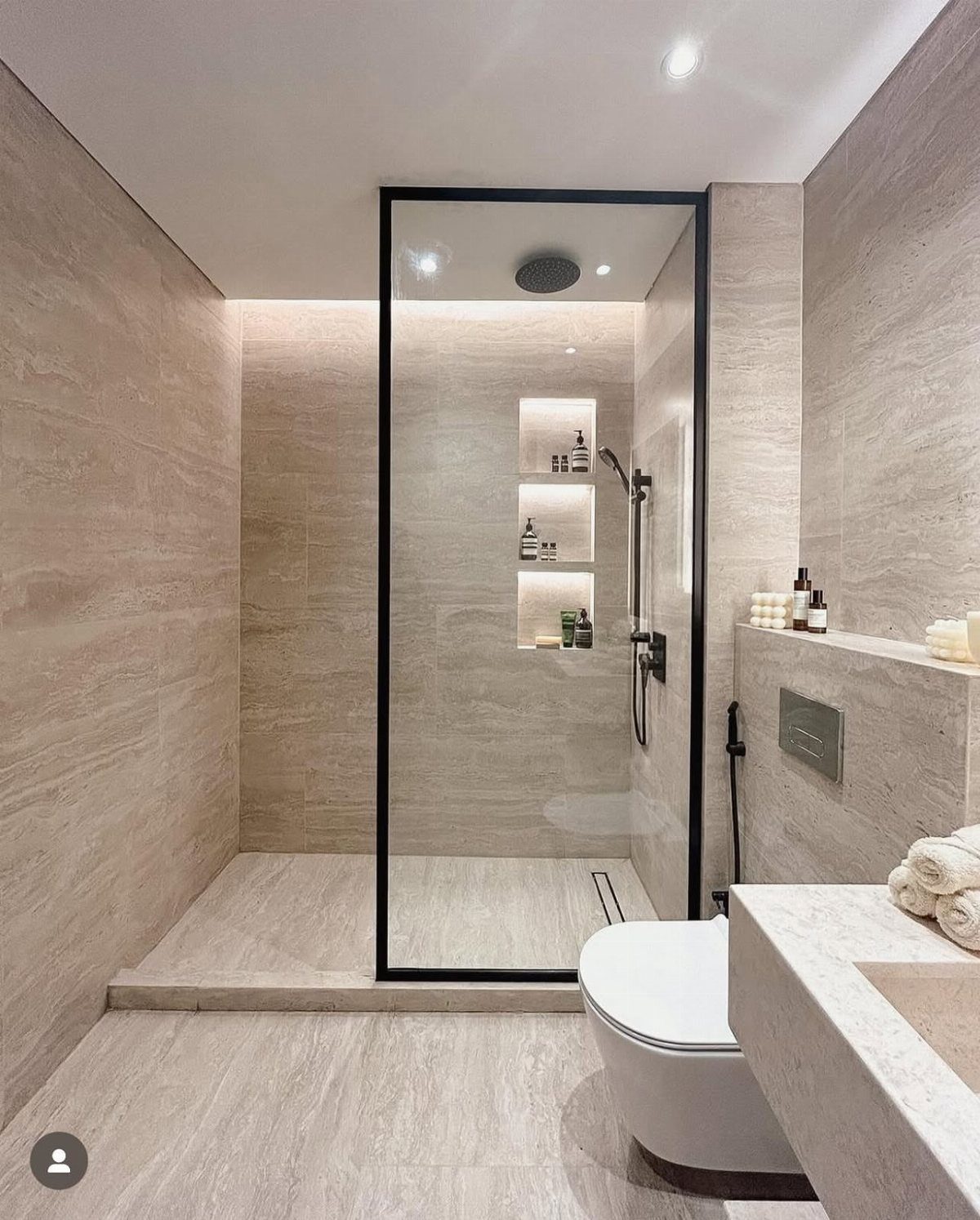 Modern walk-in shower with black-framed glass enclosure and beige stone walls.