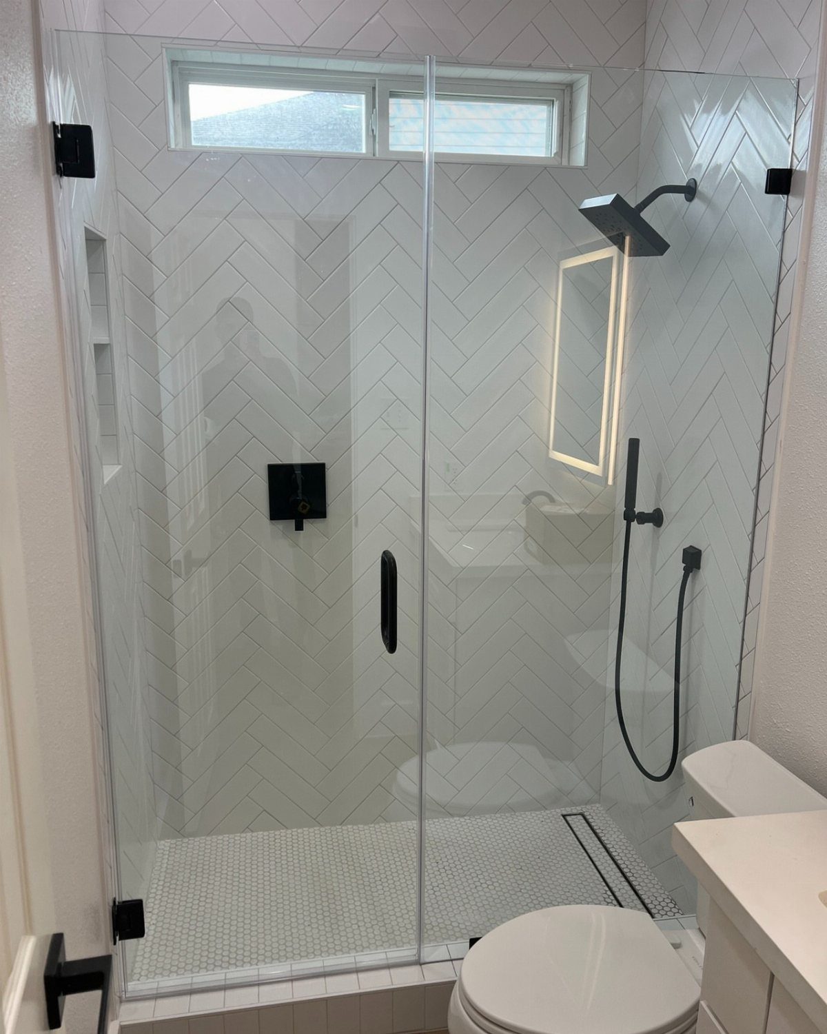 Walk-in shower with white herringbone tiles, black fixtures, and clear glass panels.