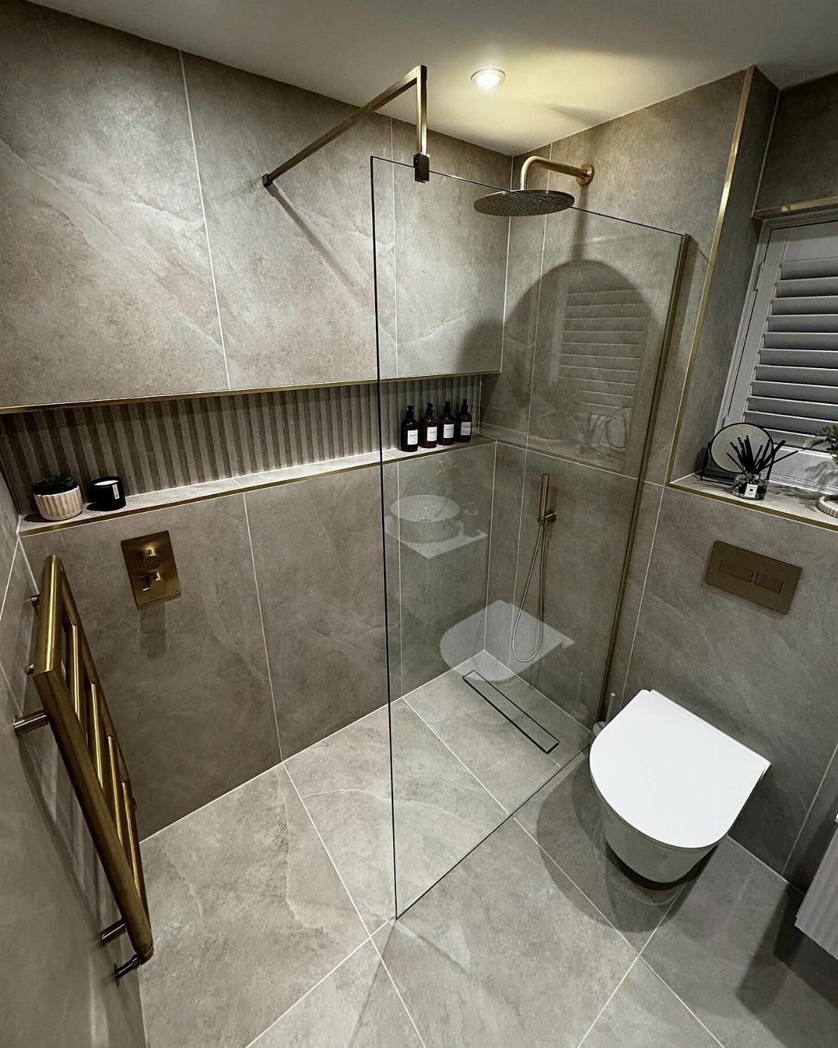 Modern walk-in shower with grey marble tiles, gold fixtures, and low-threshold entry.