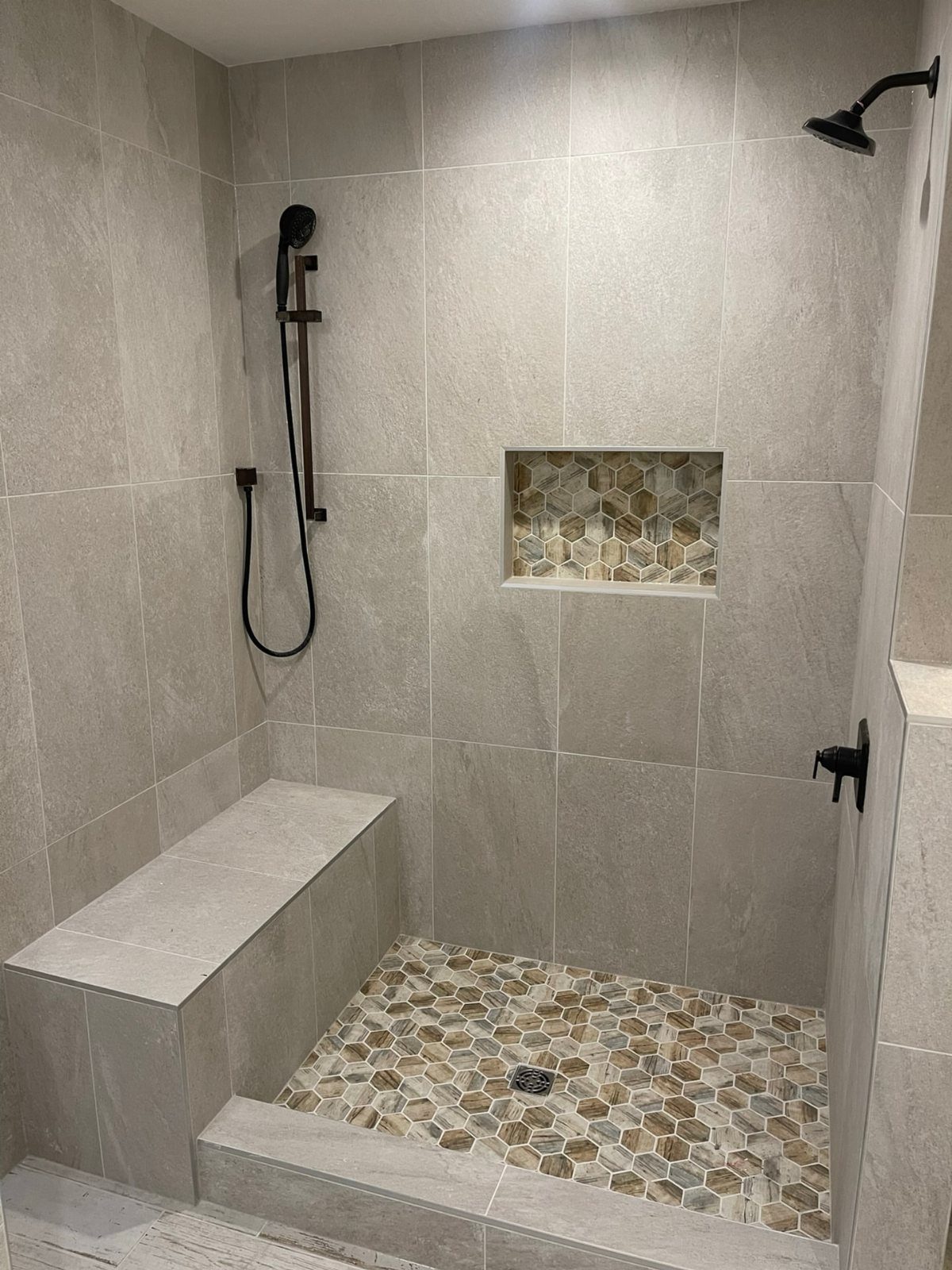 Walk-in shower featuring hexagonal mosaic tiles on the floor and in a recessed niche.