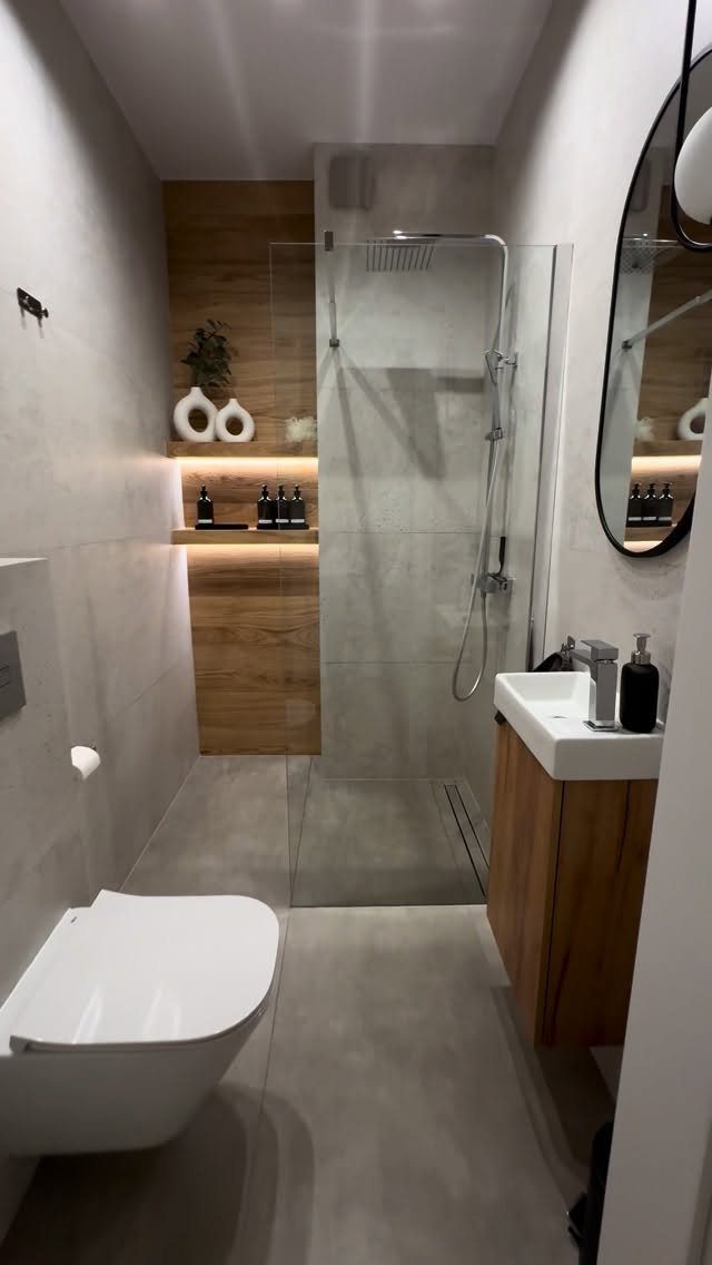 Walk-in shower in a narrow bathroom with a wooden accent wall and glass partition.