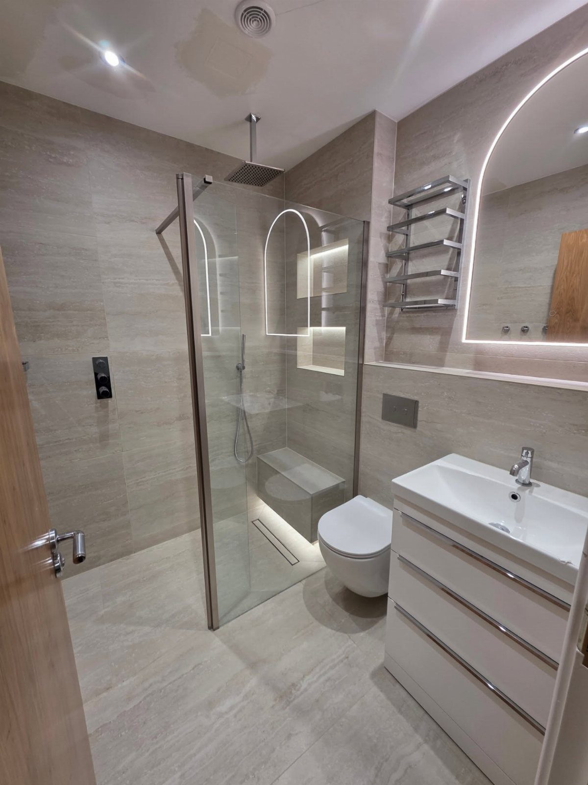 Modern bathroom with a glass walk-in shower featuring illuminated recessed wall niches.