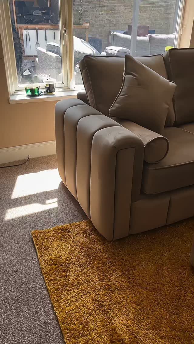 Tan chunky sofa with rounded arms next to a window and yellow rug.