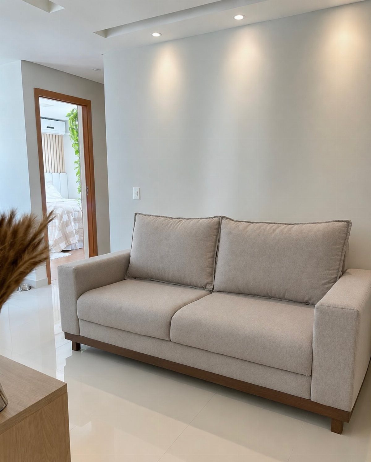 Light grey fabric two-seater sofa with wooden base against a white wall.