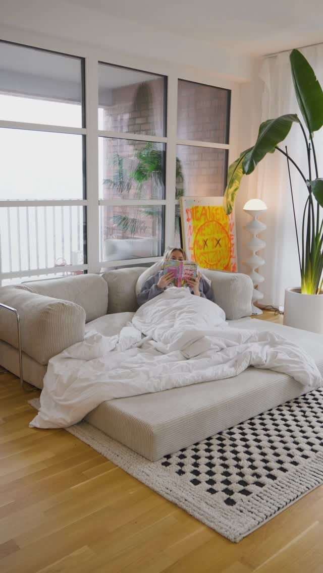 Person resting on a low beige modular sofa in a bright modern living room.