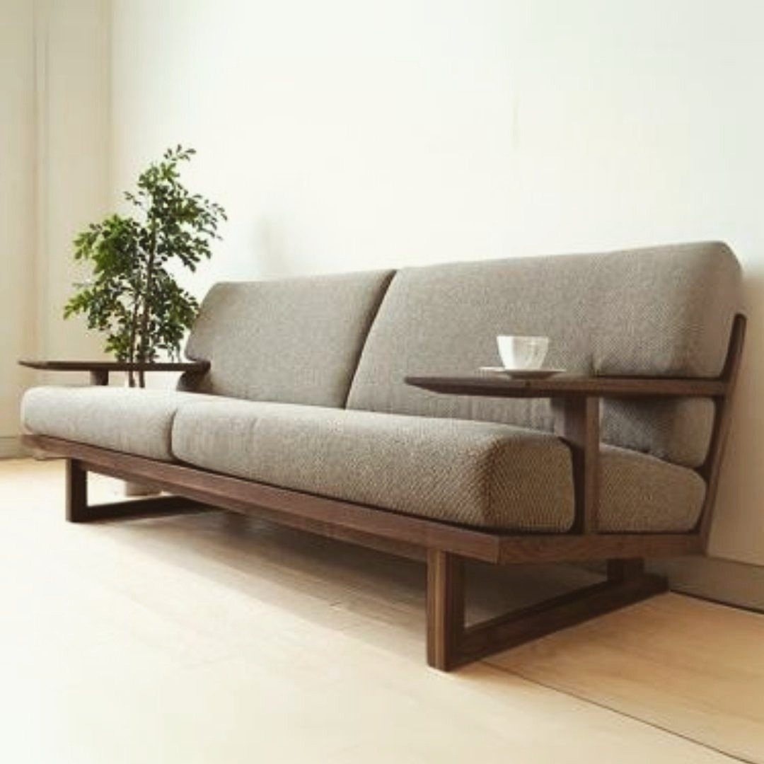 Grey fabric sofa with dark wood frame and built-in side tables in minimalist room.