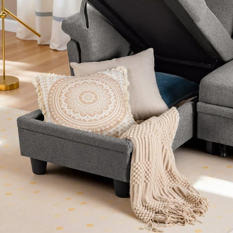 Grey storage sofa with lifted seat showing pillows and a beige knit throw blanket