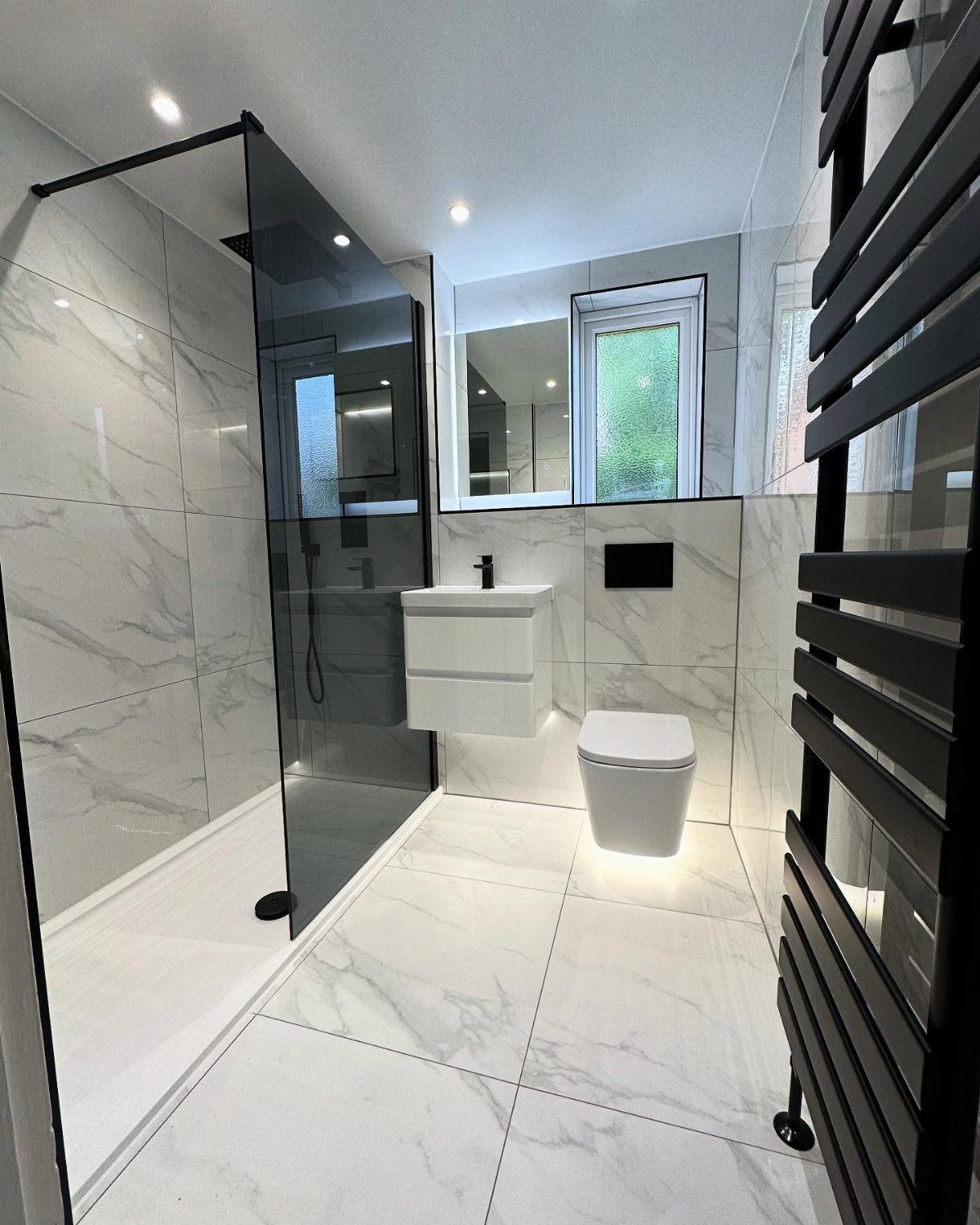 Modern bathroom with white marble tiles, black fixtures, and a glass walk-in shower.