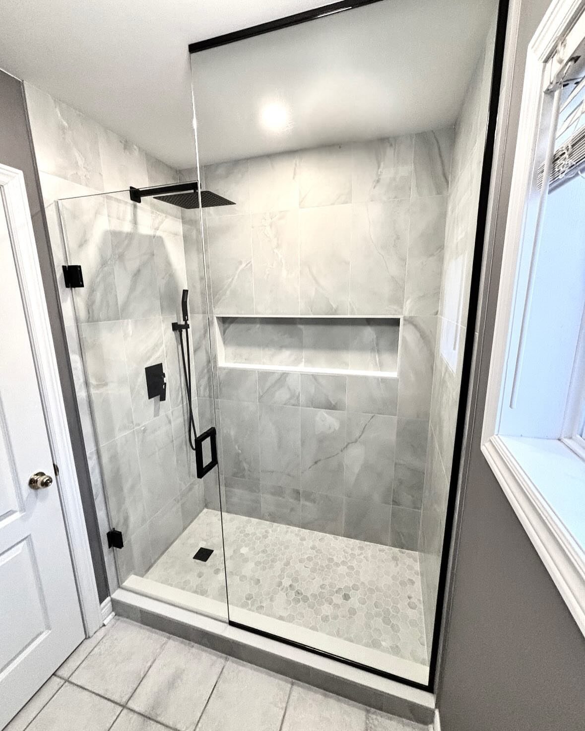 Walk-in shower with white marble tiles and a built-in recessed wall shelf niche.
