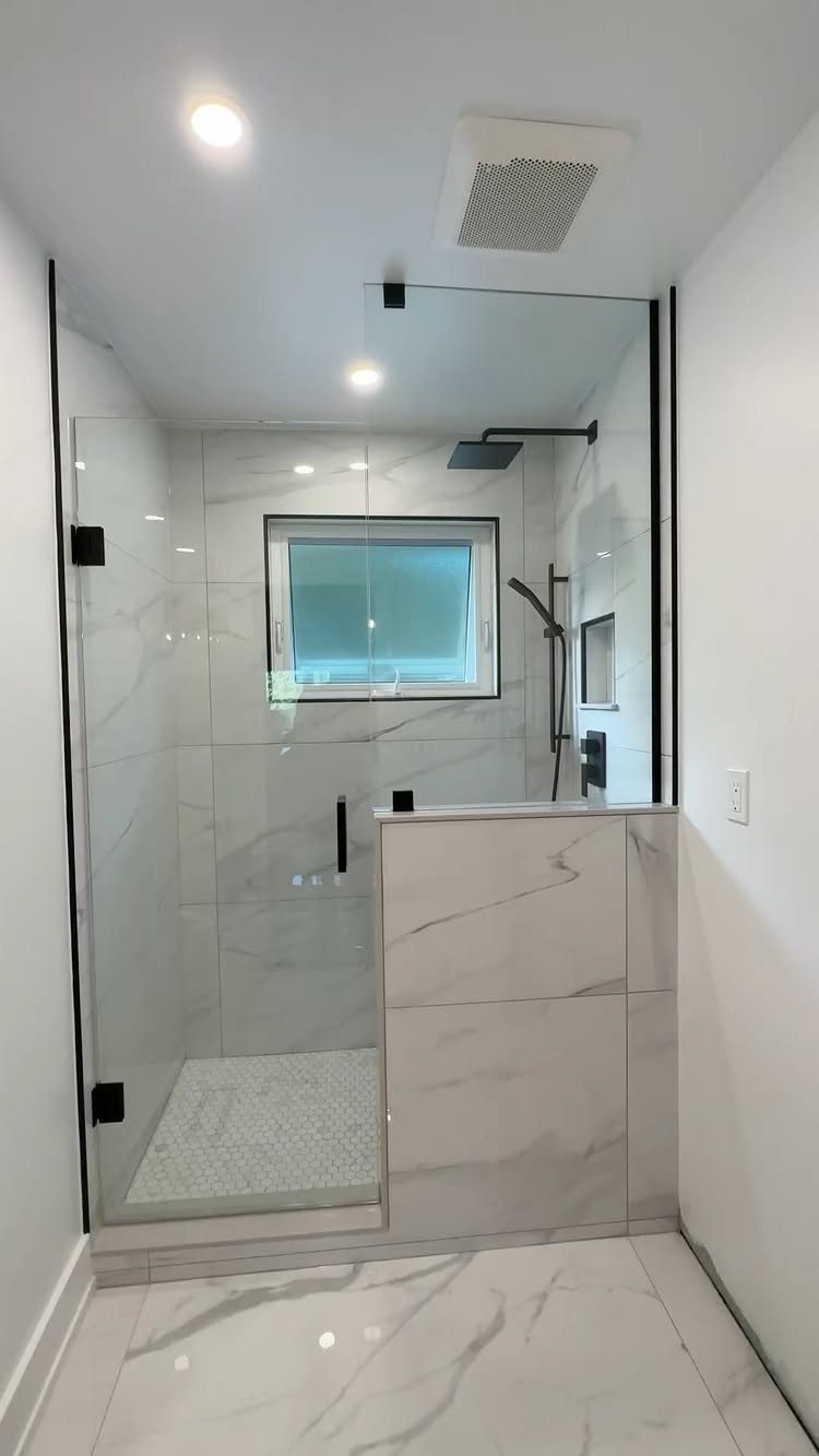 Modern walk-in shower with frameless glass enclosure and white marble tiles.