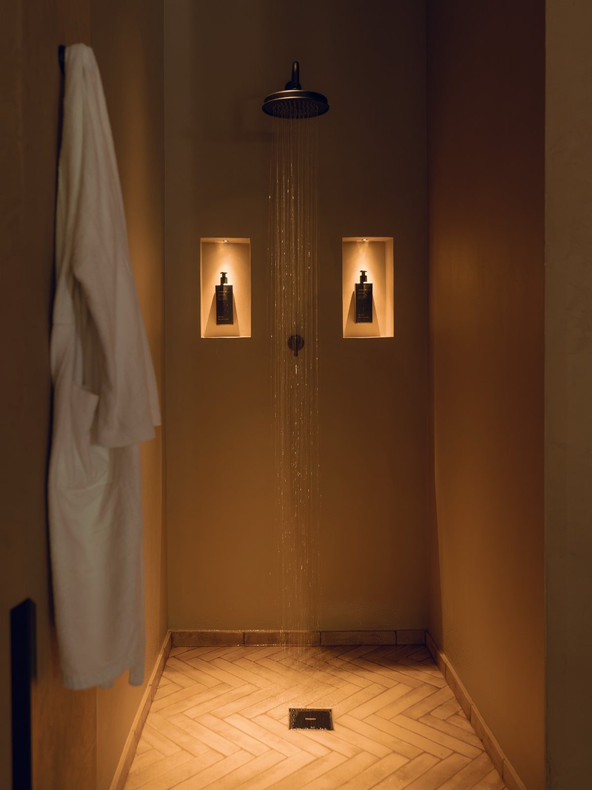 Walk-in shower with rain showerhead, illuminated niches, and herringbone tiled floor.
