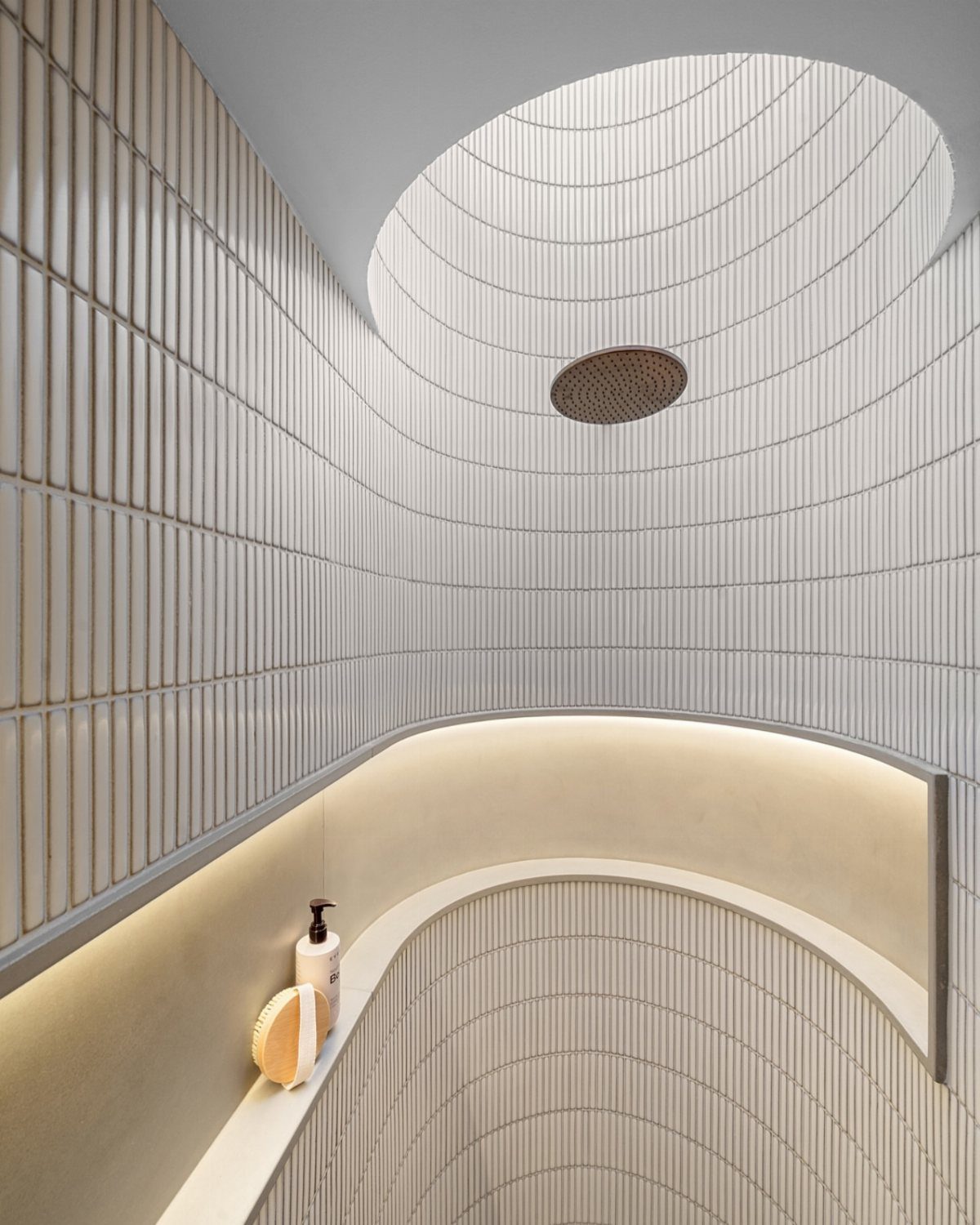 Curved shower walls with white ribbed tiles and a circular rain showerhead.