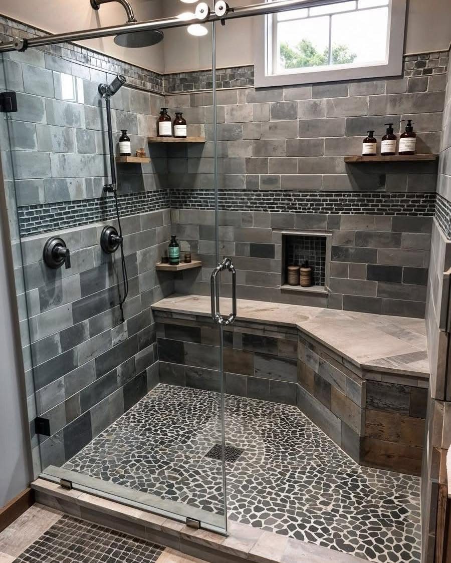 Built-in L-shaped stone shower seat in a grey tiled walk-in shower with glass door.