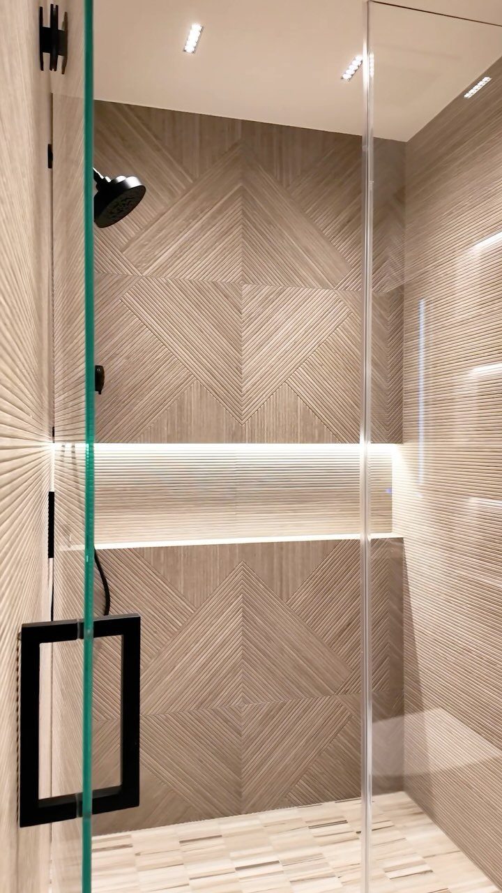 Modern walk-in shower featuring beige textured tiles in a geometric pattern and glass walls.