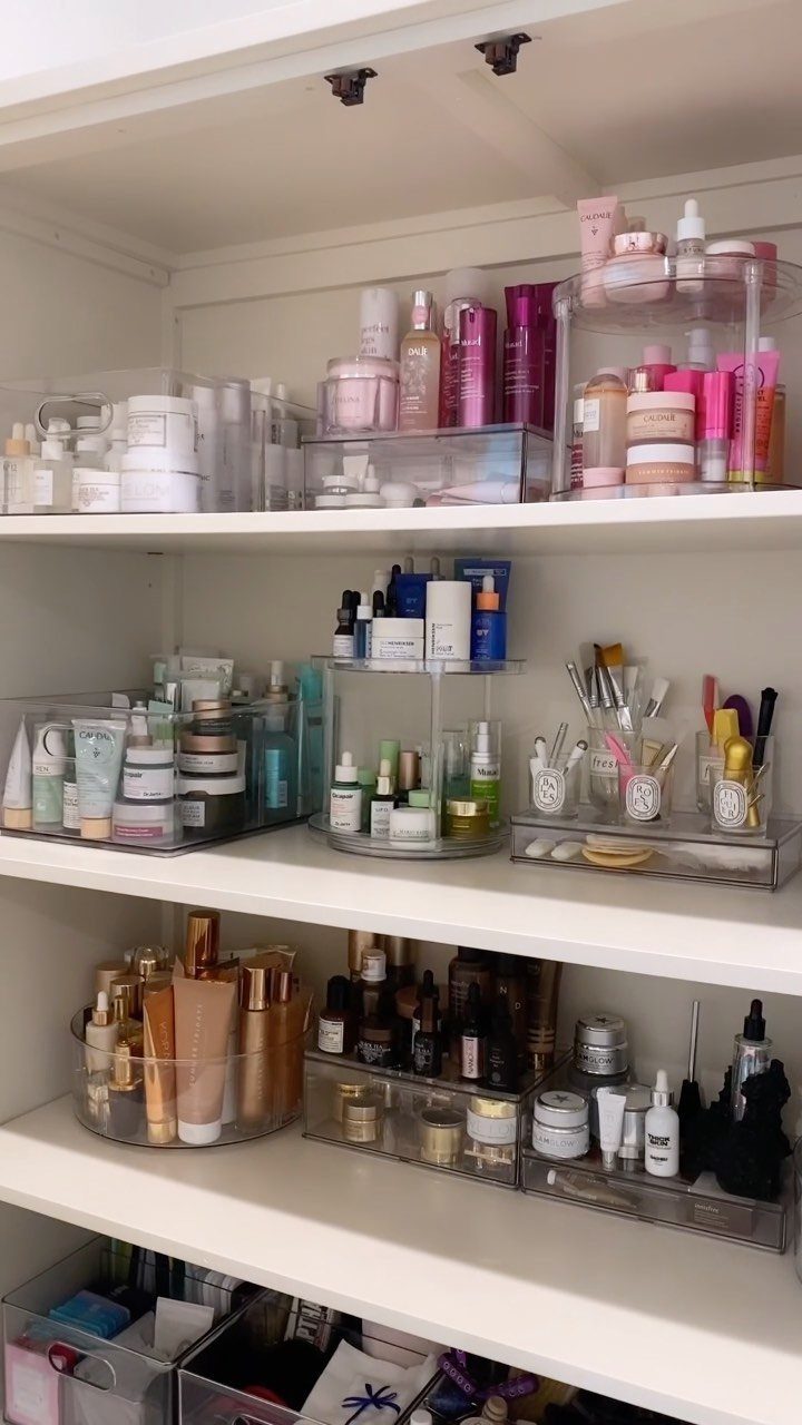 Skincare and makeup products organized in clear acrylic bins on white shelves.