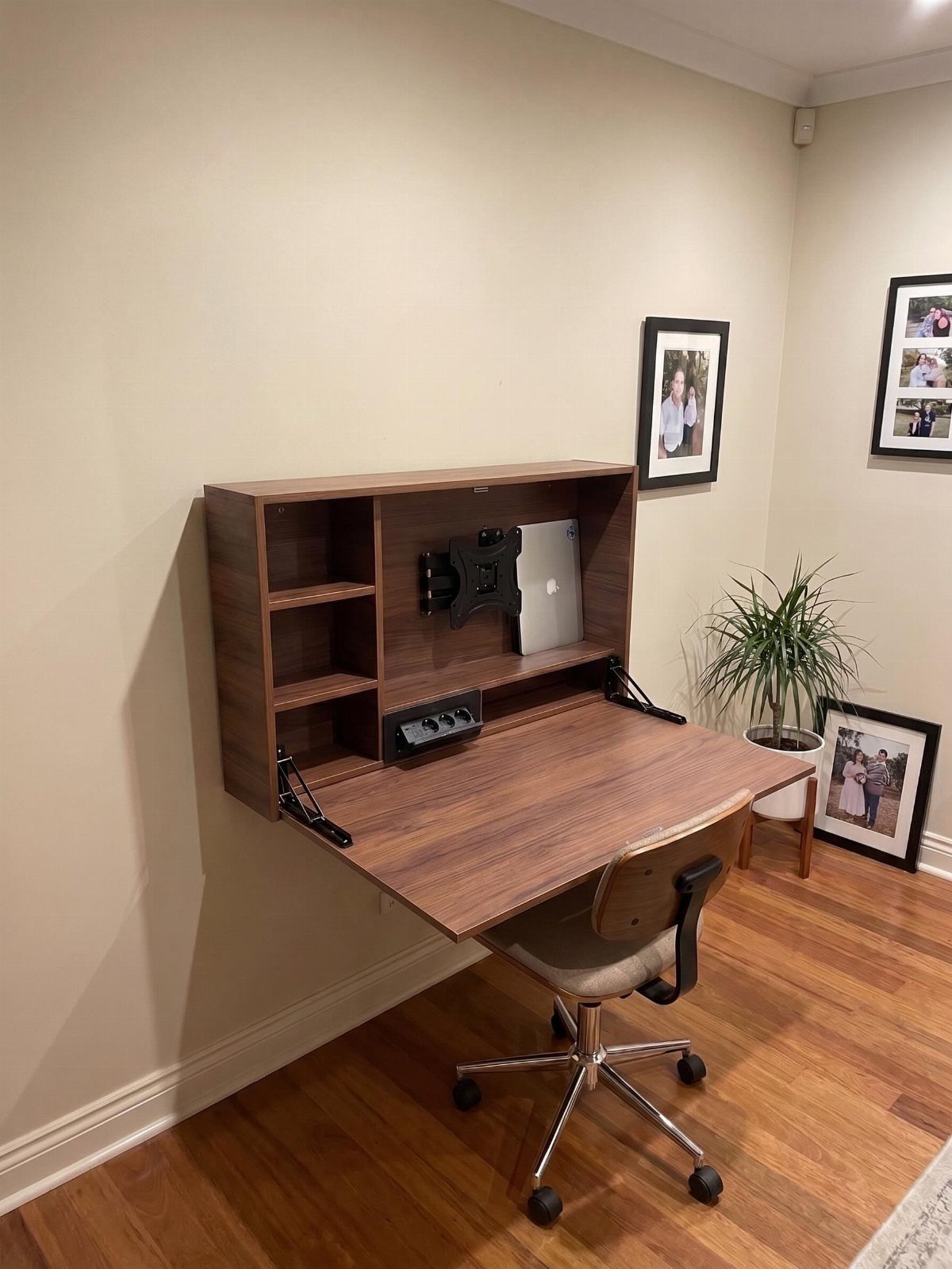 Wall-mounted wooden folding desk with built-in shelving and a beige office chair.