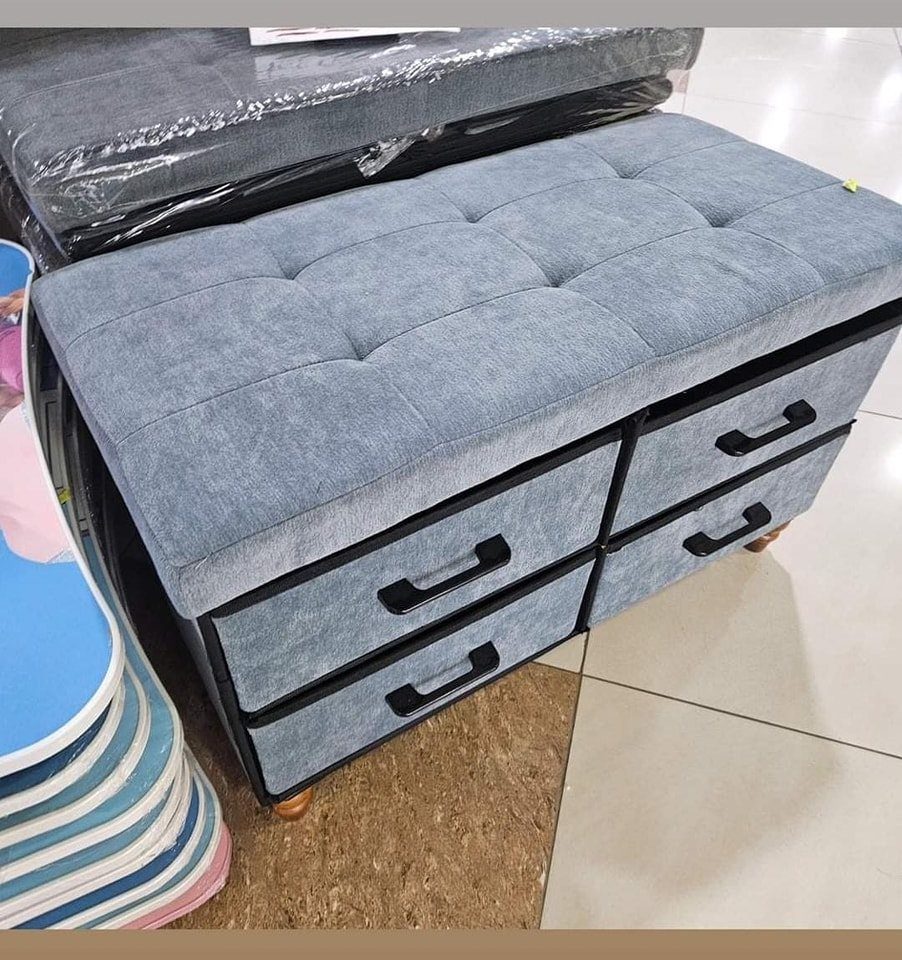 Grey tufted storage ottoman with four drawers and black handles in a store.