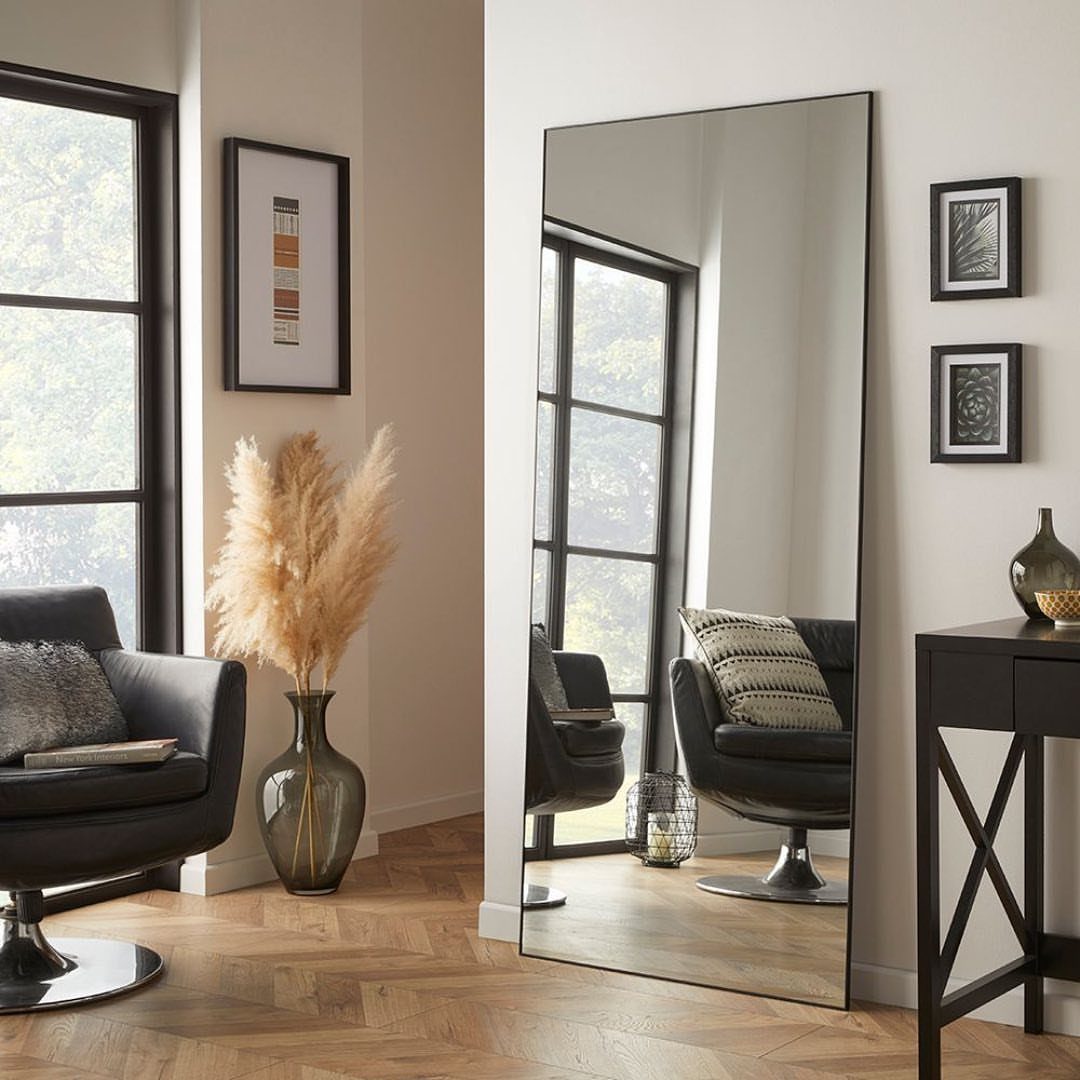 Large rectangular mirror leaning against a white wall in a modern living room