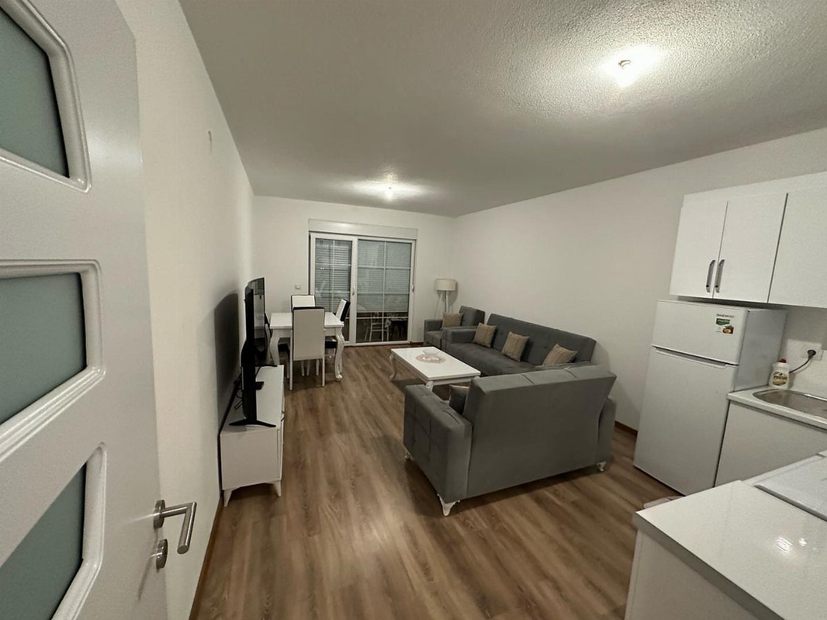 Studio apartment interior with white walls, grey sofa, and light wood floors.