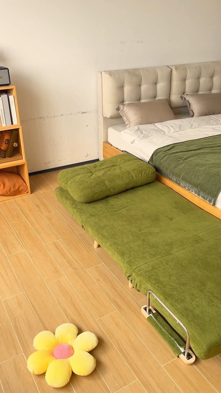 Green foldable guest bed extended on a light wood floor in a bedroom.