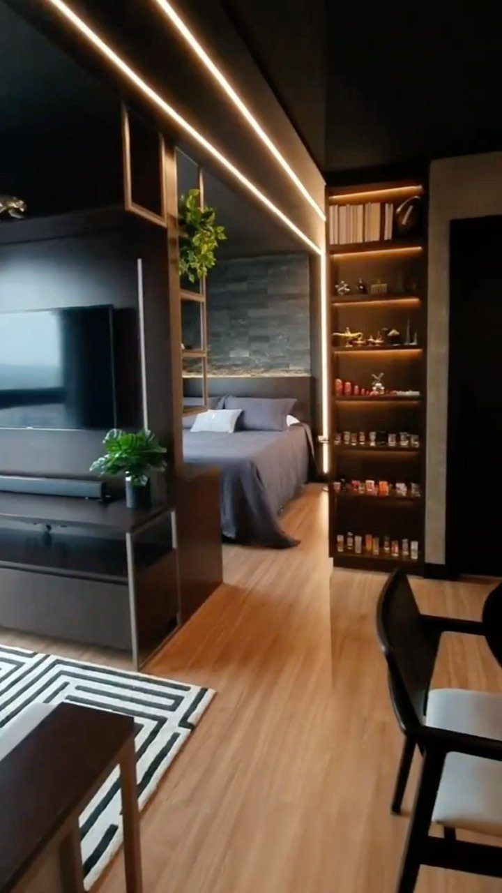 Modern studio apartment interior with dark wood furniture and a tall illuminated bookshelf.